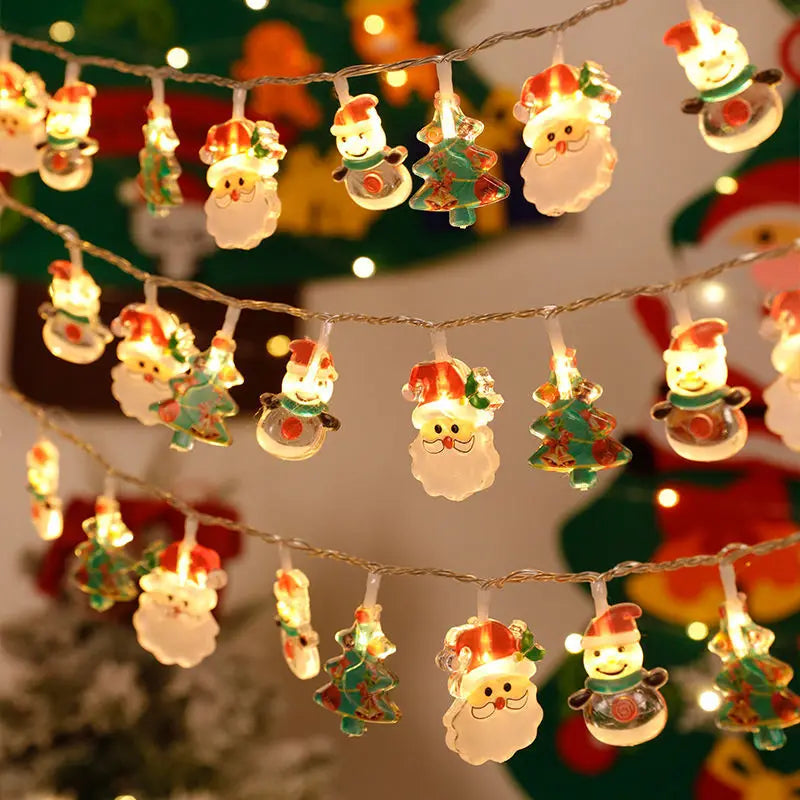 Festive string lights featuring illuminated Santa heads, snowmen, and Christmas trees hanging in rows, casting a warm, cheerful glow.