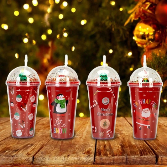 Four red Christmas-themed cups with straws, decorated with Santa, penguins, and festive phrases like "Let it Snow" and "Merry Christmas." Soft, golden lights twinkle in the background.