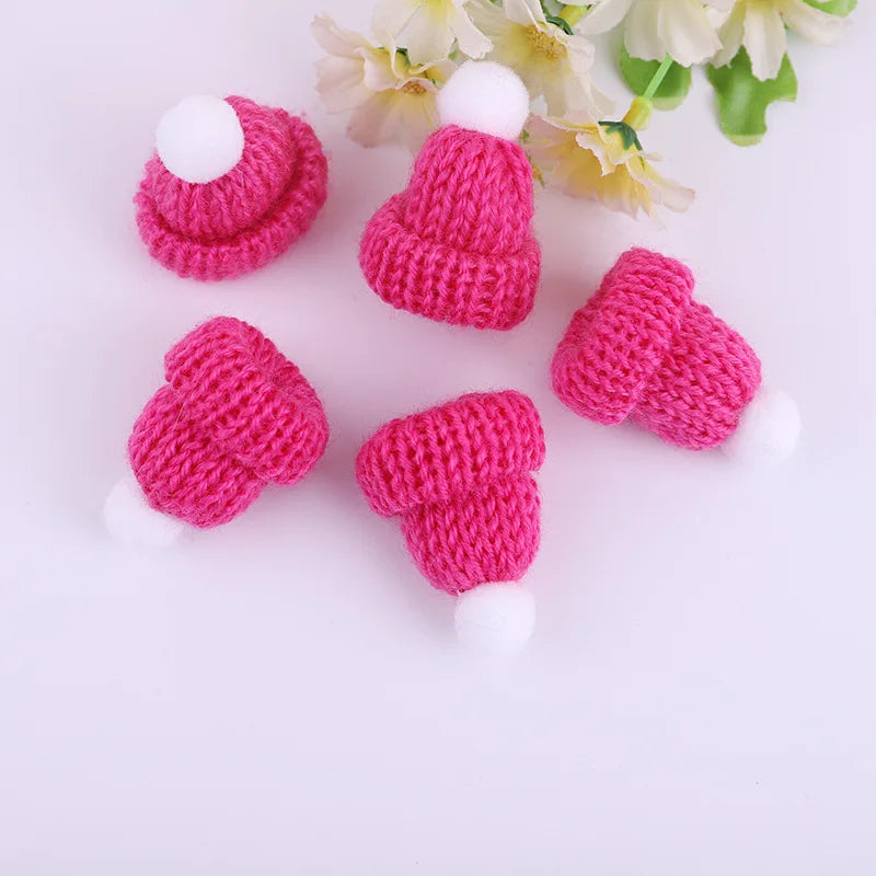 Five miniature pink knitted hats with white pom-poms arranged in a semi-circle on a white surface, accompanied by pale yellow flowers in the background.