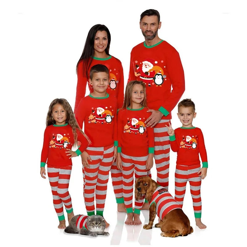 Family and pets in matching red and gray striped Christmas pajamas with Santa and penguin designs. The group includes two adults, four children, a gray cat, and a brown dog.