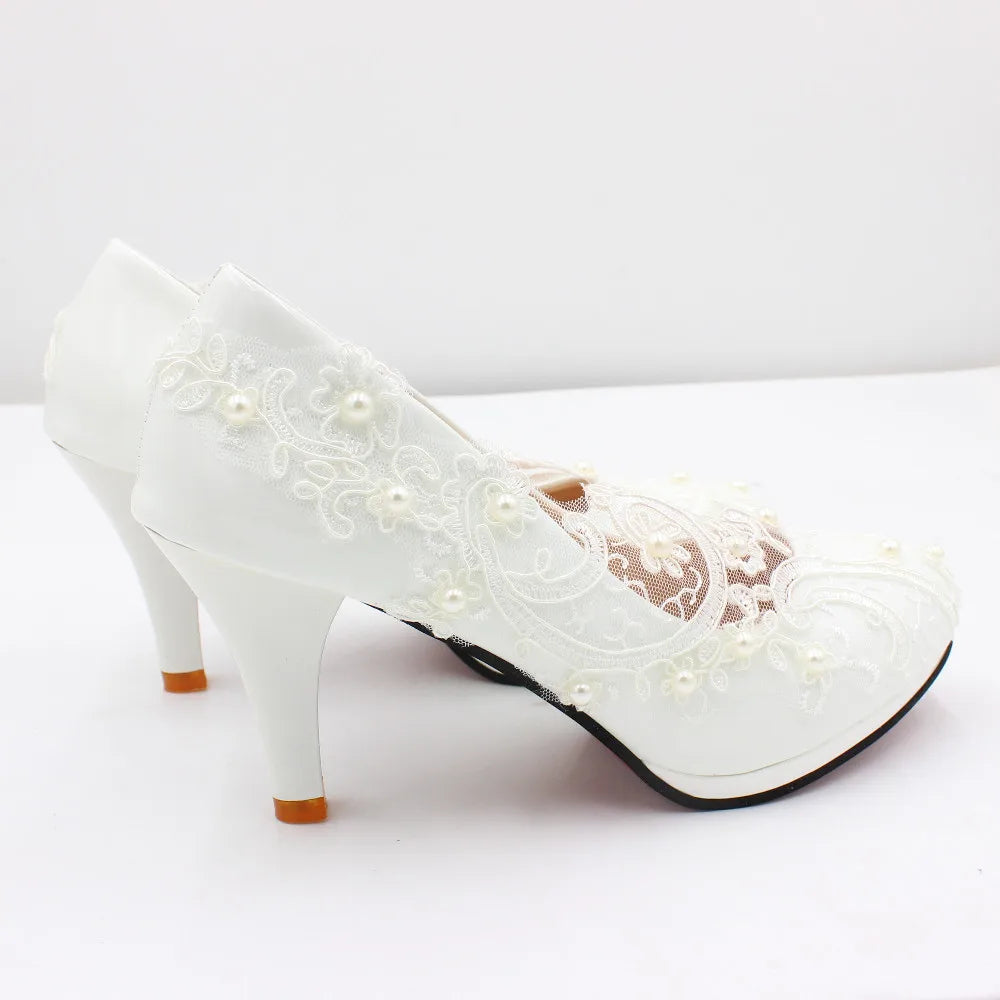 White high-heeled shoes with lace and pearl embellishments on a plain background, showcasing elegant floral patterns and intricate design details.