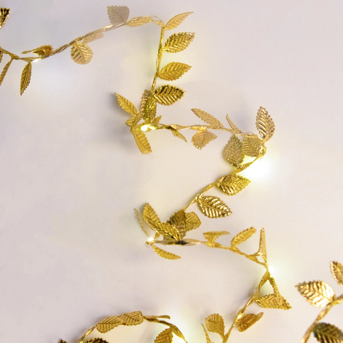 Golden decorative leaf garland with small LED lights intertwined, creating an elegant zigzag pattern against a plain white background.