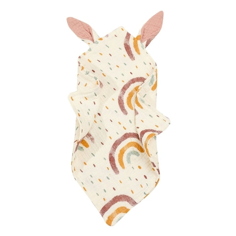 Soft baby comforter with pastel rainbows and dots on a cream background, featuring two pink ears at the top. The fabric appears to be light and crumpled.