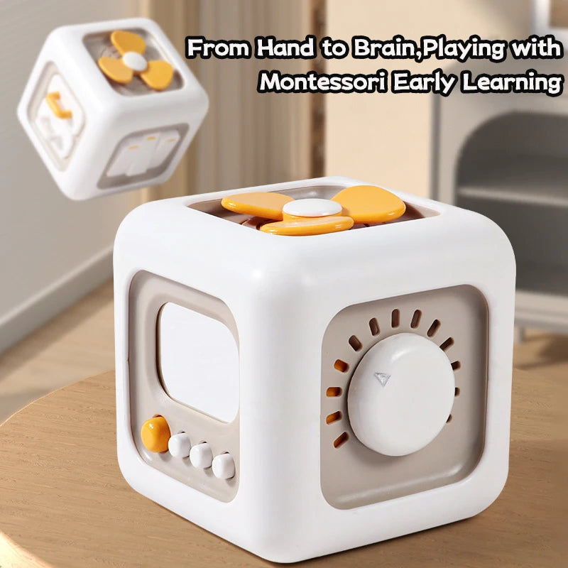 White and beige Montessori cube toy with interactive dials, buttons, and a yellow propeller on a wooden surface. Text reads, "From Hand to Brain, Playing with Montessori Early Learning."