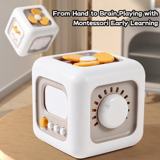 White and beige Montessori cube toy with interactive dials, buttons, and a yellow propeller on a wooden surface. Text reads, "From Hand to Brain, Playing with Montessori Early Learning."