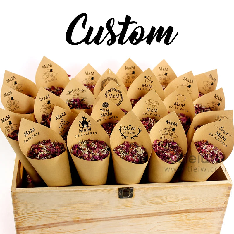 Custom paper cones filled with dried flower petals, arranged in a wooden box. Each cone displays a wedding date and initials "M&M" with various decorative icons.