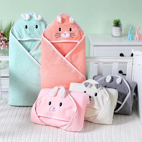 Pastel-colored baby hooded towels shaped like animals are displayed on a bed and dresser. Designs include a mint elephant and peach, pink, ivory, and gray bunnies.