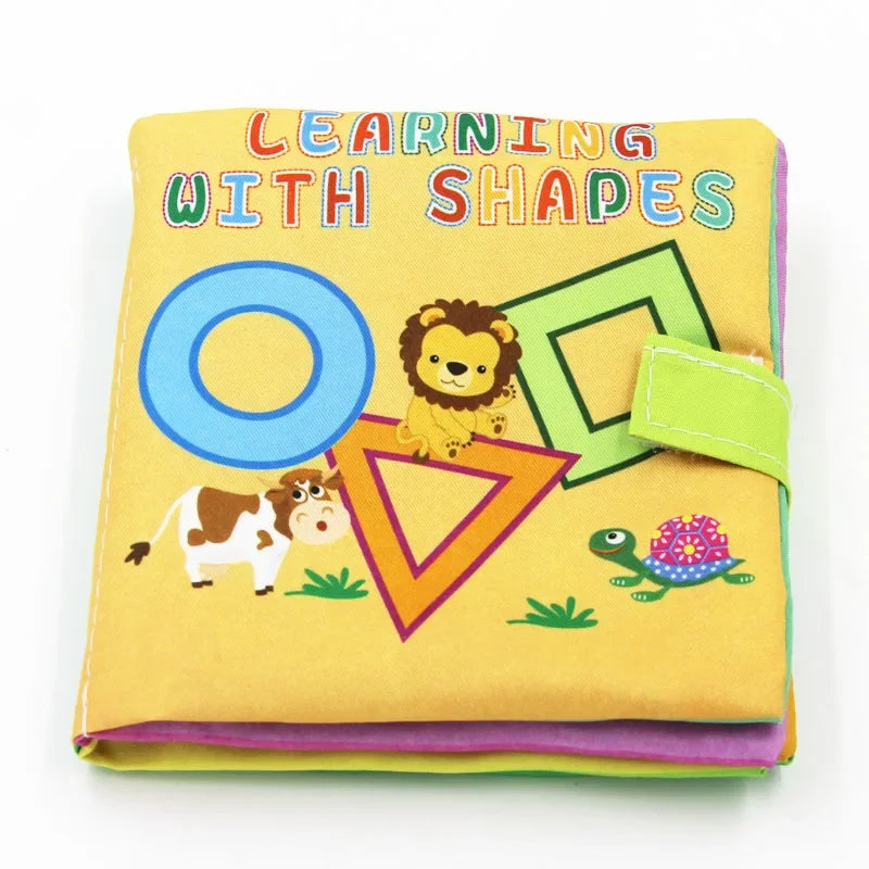 Children's fabric book titled "Learning with Shapes" featuring colorful geometric shapes and cartoon animals like a lion, cow, and turtle on the cover, secured with a green strap.