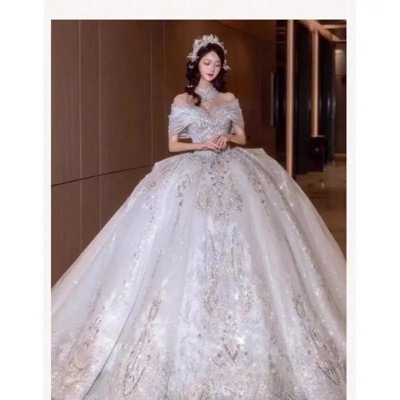 A woman in an elegant, off-shoulder gown adorned with intricate silver embellishments and a voluminous skirt, standing in a softly lit hallway, wearing a decorative headpiece.