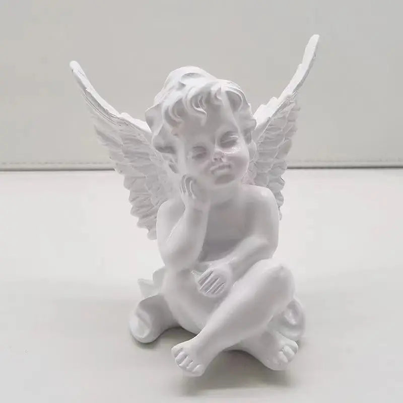 White cherub figurine with detailed wings and curly hair. The cherub is seated with one hand resting on its cheek, exuding a peaceful and contemplative expression.