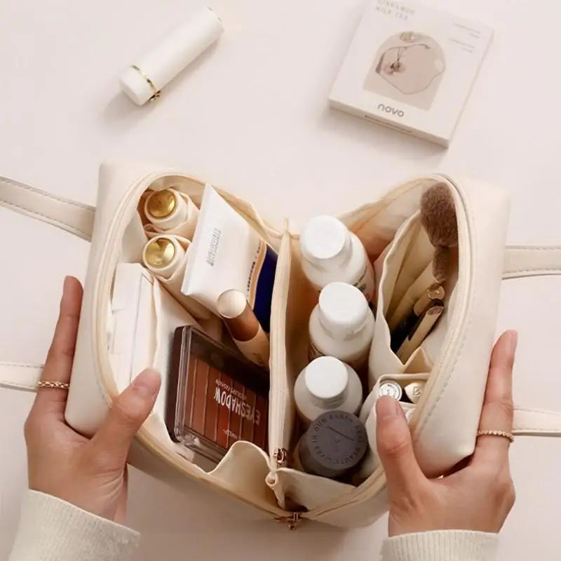 Cream-colored makeup bag open, revealing skincare bottles, makeup items like brushes, eyeshadow palette, and other beauty essentials. Two hands hold the bag open.