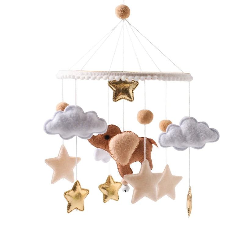 Baby mobile with felt clouds, stars, and an elephant hanging from a round frame. The colors include gold, beige, and gray, creating a whimsical nursery decoration.