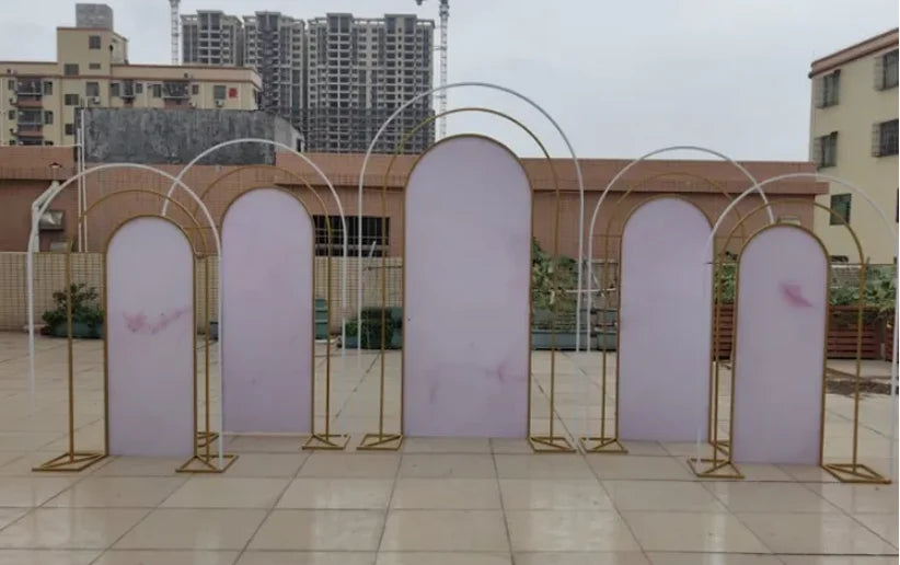 Modern outdoor backdrop with overlapping pink arches set against a tiled floor. Tall buildings and a cloudy sky form the urban background.