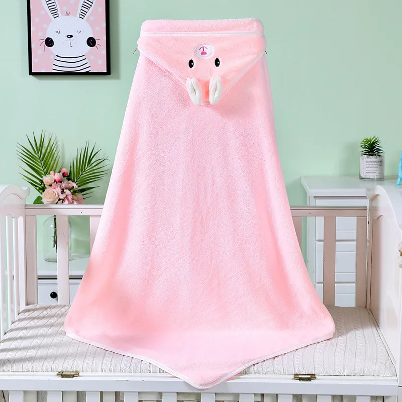 A pink hooded towel with a bunny design on the hood is draped over a crib. The wall is light green, with a framed bunny picture and decorative plants in the background.