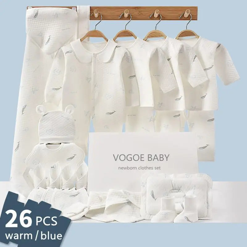 White 26-piece newborn clothes set hangs on wooden rack against a blue background. Includes tops, pants, hat, and blanket, with "Vogoe Baby" packaging visible.