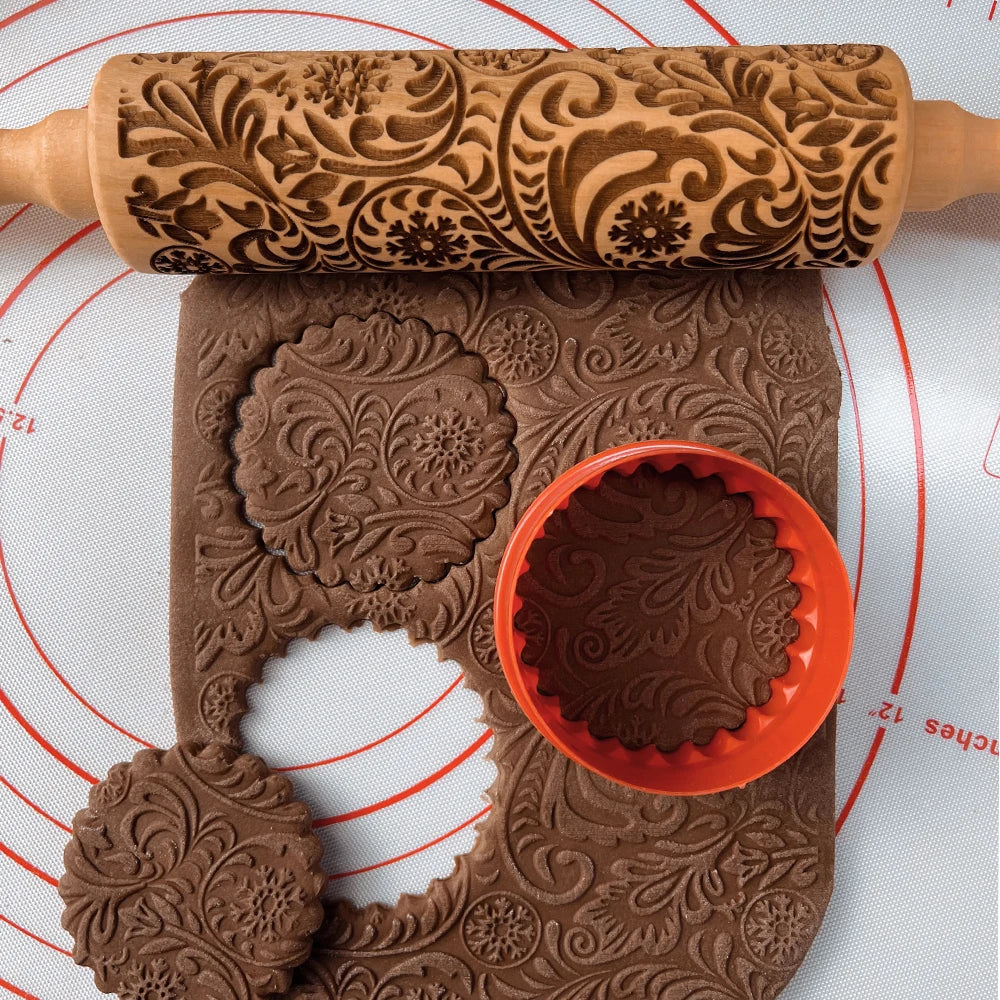 Embossed rolling pin with intricate floral patterns, used to create textured chocolate dough. A red cookie cutter is shown creating round cookie shapes on a marked baking mat.