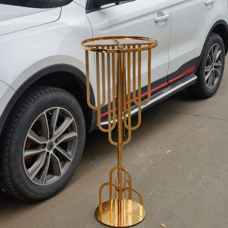 A gold metal stand with an intricate design next to the rear wheel of a white car on a concrete surface.