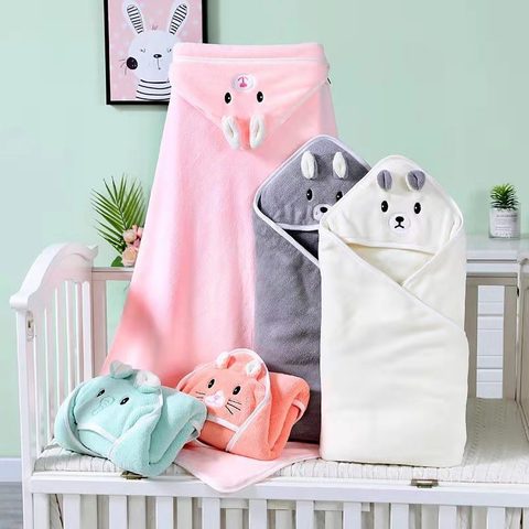 Soft hooded baby towels shaped like animals in pastel colors are arranged on a crib. There's a pink, grey, cream, and mint green towel, each with cute embroidered faces.