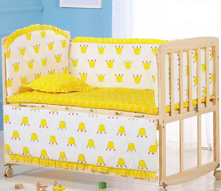 Wooden baby crib with yellow and white bedding, adorned with playful crown patterns. The crib is set against a light blue wall and white curtains, creating a bright nursery scene.