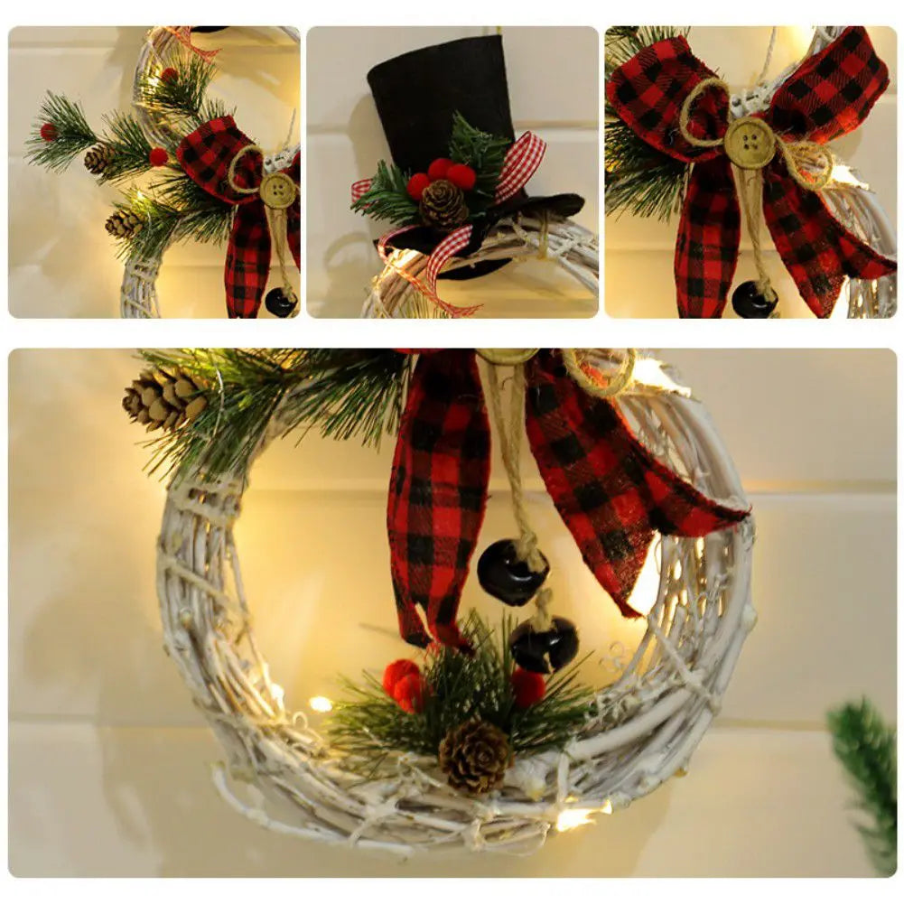 Wicker wreath adorned with a red and black plaid bow, pinecones, greenery, red berries, and black bells. A black top hat sits on one section. Warm lights illuminate it.