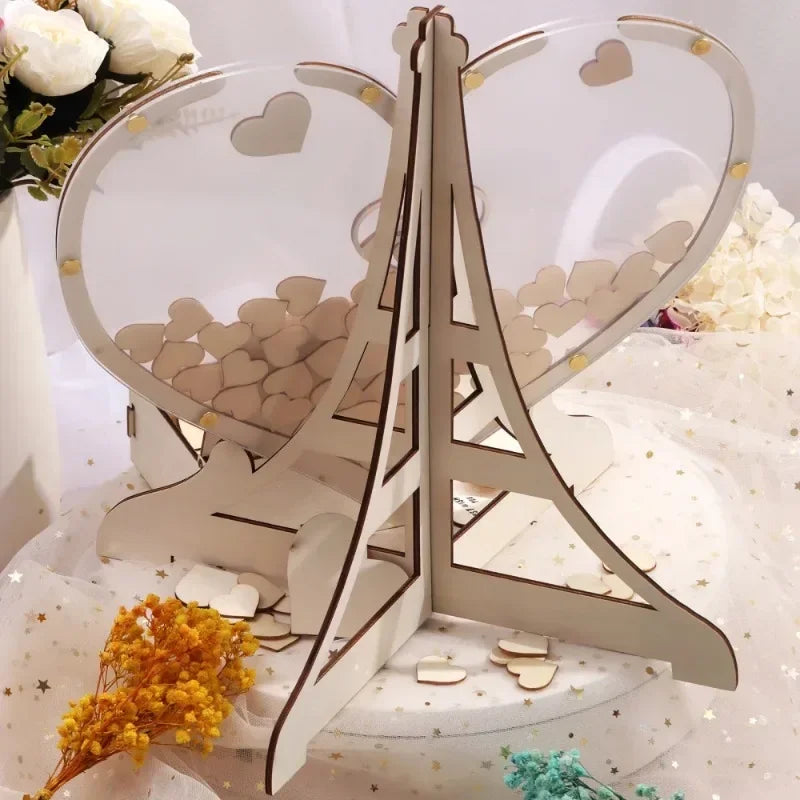 Heart-shaped acrylic guestbook with small wooden hearts inside, framed by an Eiffel Tower design. Decorated with flowers, set on a white and star-patterned background.