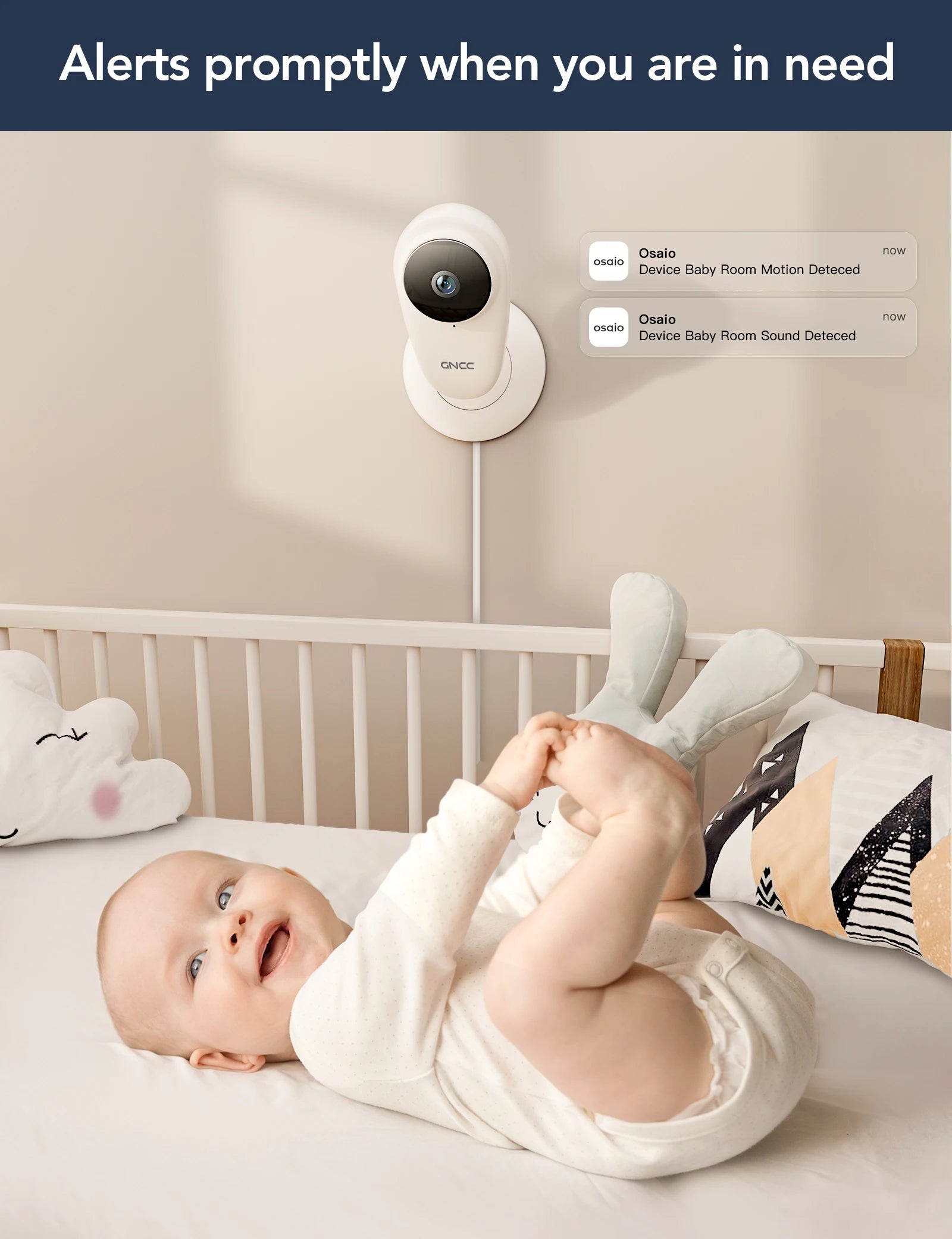 A baby in a crib smiles while a wall-mounted camera sends alerts for motion and sound detection. Two cloud pillows and a patterned pillow are visible in the crib.