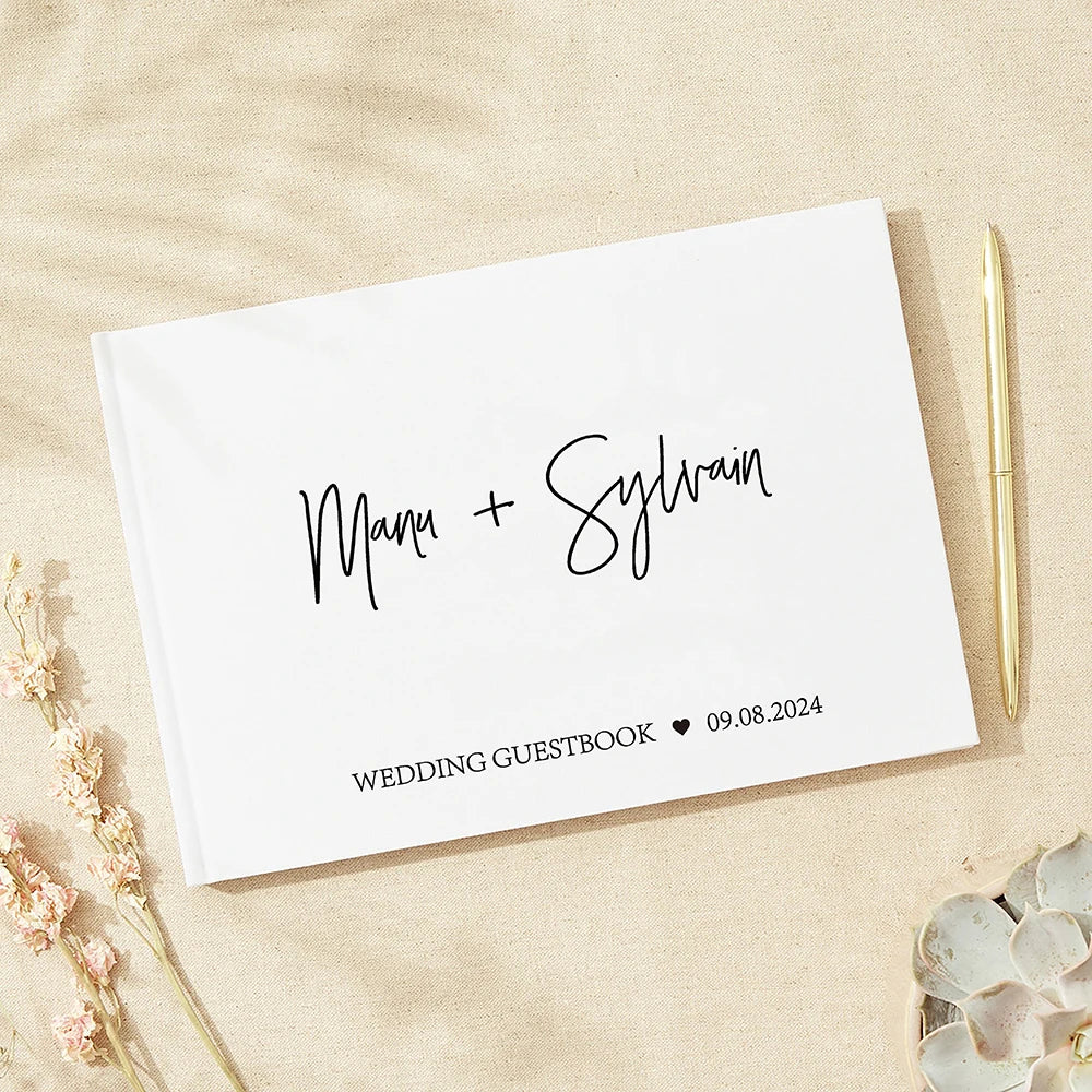 White wedding guestbook with "Mari + Sylvain" in cursive. Gold pen and dried flowers are nearby on a beige background. Date: 09.08.2024.