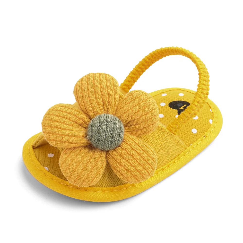 Yellow baby sandal with a soft, textured flower on top and a polka dot footbed. The sandal has a flexible heel strap, designed for infants.