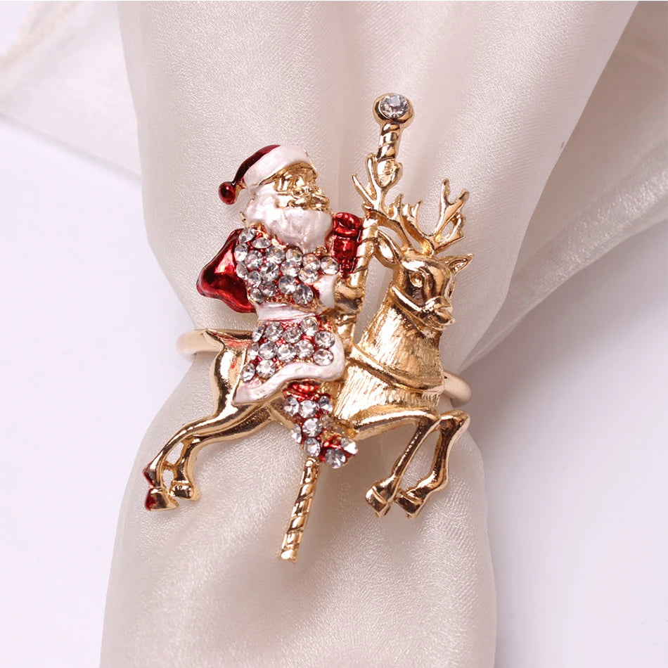 A sparkling, jeweled brooch depicting Santa Claus riding a golden reindeer, adorned with red and clear crystals. It rests on a smooth, satin-like white fabric.
