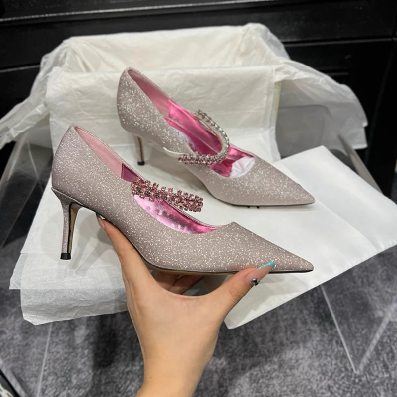 Sparkly beige stiletto heels with rhinestone embellishment and pink satin interior, held by a hand above a tissue-lined shoebox.