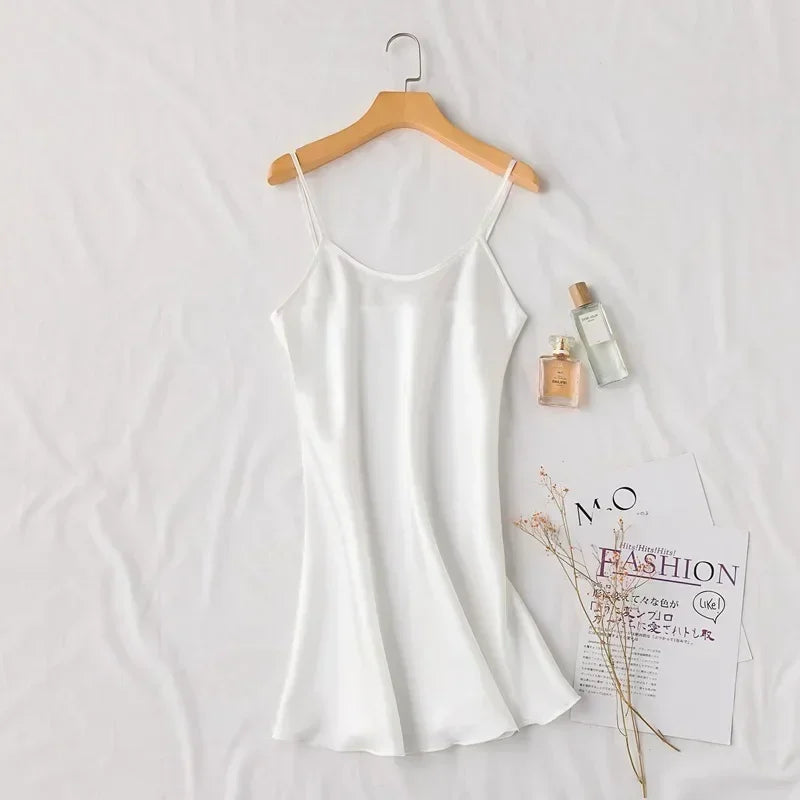 Silky white slip dress on a hanger, surrounded by two perfume bottles, dried flowers, and fashion magazines, creating an elegant and minimalist aesthetic.