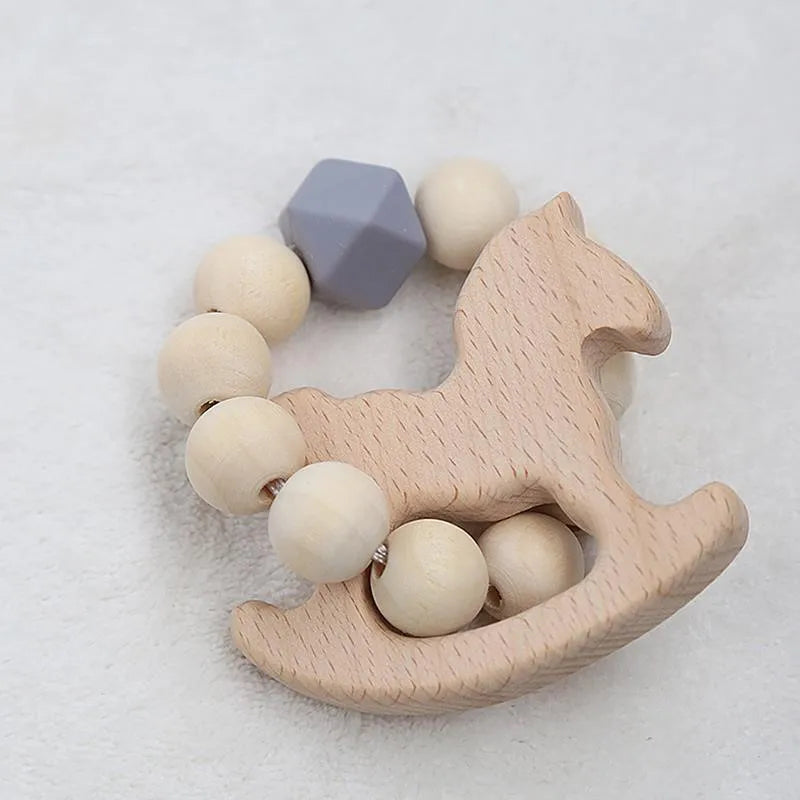 Wooden teething ring featuring a beaded circle with natural and blue beads, and a rocking horse shape. Placed on a soft, gray textured surface.