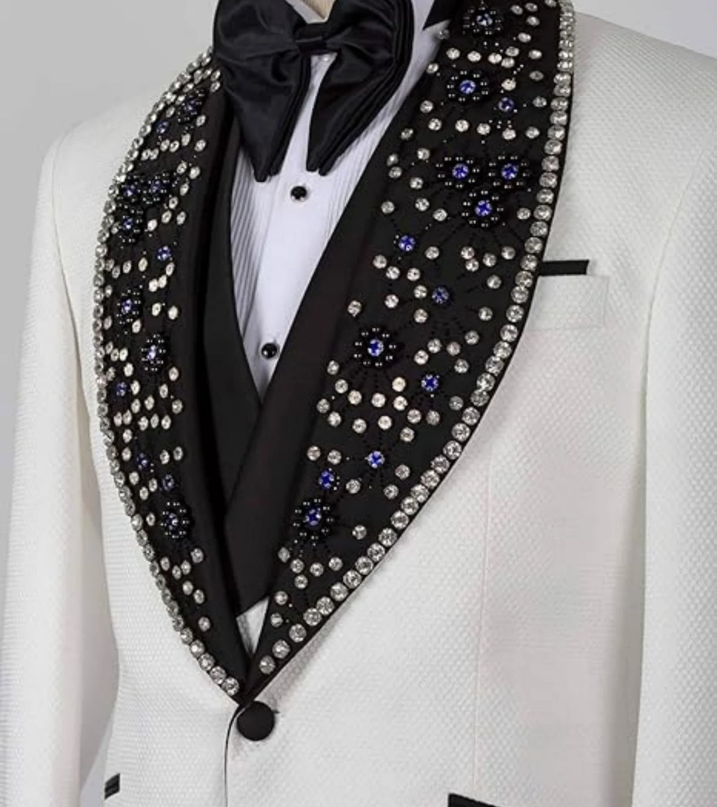 White tuxedo with a black lapel adorned with sparkling rhinestones and blue gems, paired with a black bow tie.