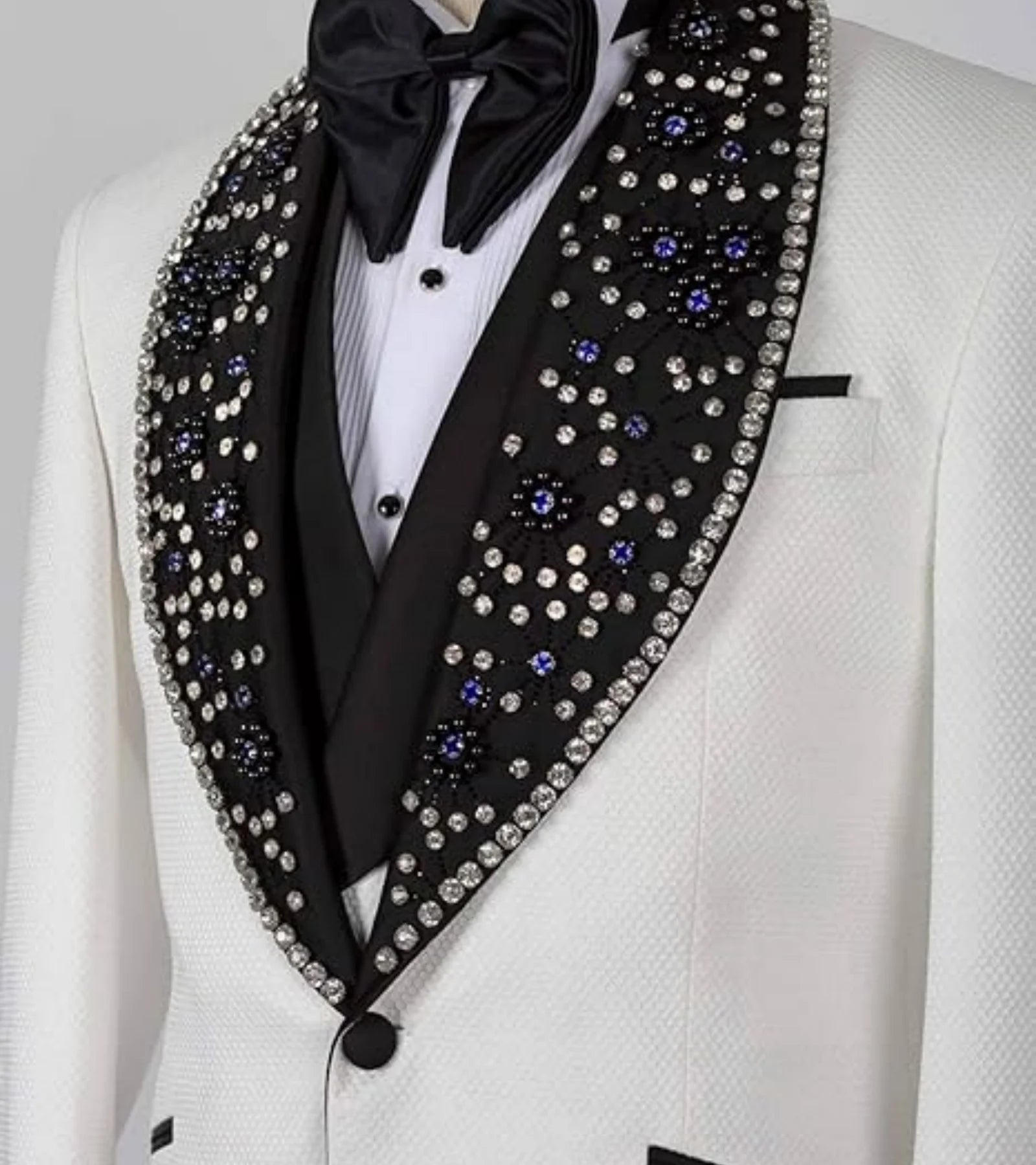 White tuxedo with a black lapel adorned with sparkling rhinestones and blue gems, paired with a black bow tie.