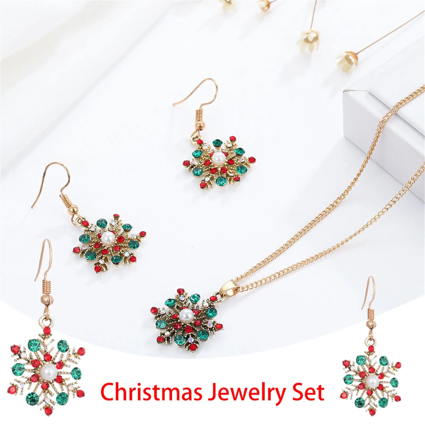 Christmas jewelry set with gold chain necklace and matching earrings, adorned with red and green gemstones, arranged in a festive star pattern on a white background.