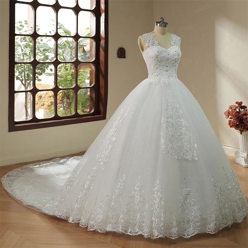 Elegant white wedding gown on a mannequin, featuring intricate lace details and a long train. Displayed by a window with natural light highlighting the dress's texture and design.