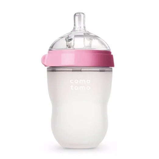 A pink-lidded baby bottle with a silicone teat and contoured design for easy gripping, labeled "comotomo."