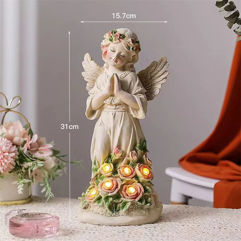 Angel statue with floral design, measuring 31 cm tall and 15.7 cm wide. The flowers are illuminated with small lights. Decor with pink flowers and a red cloth in the background.