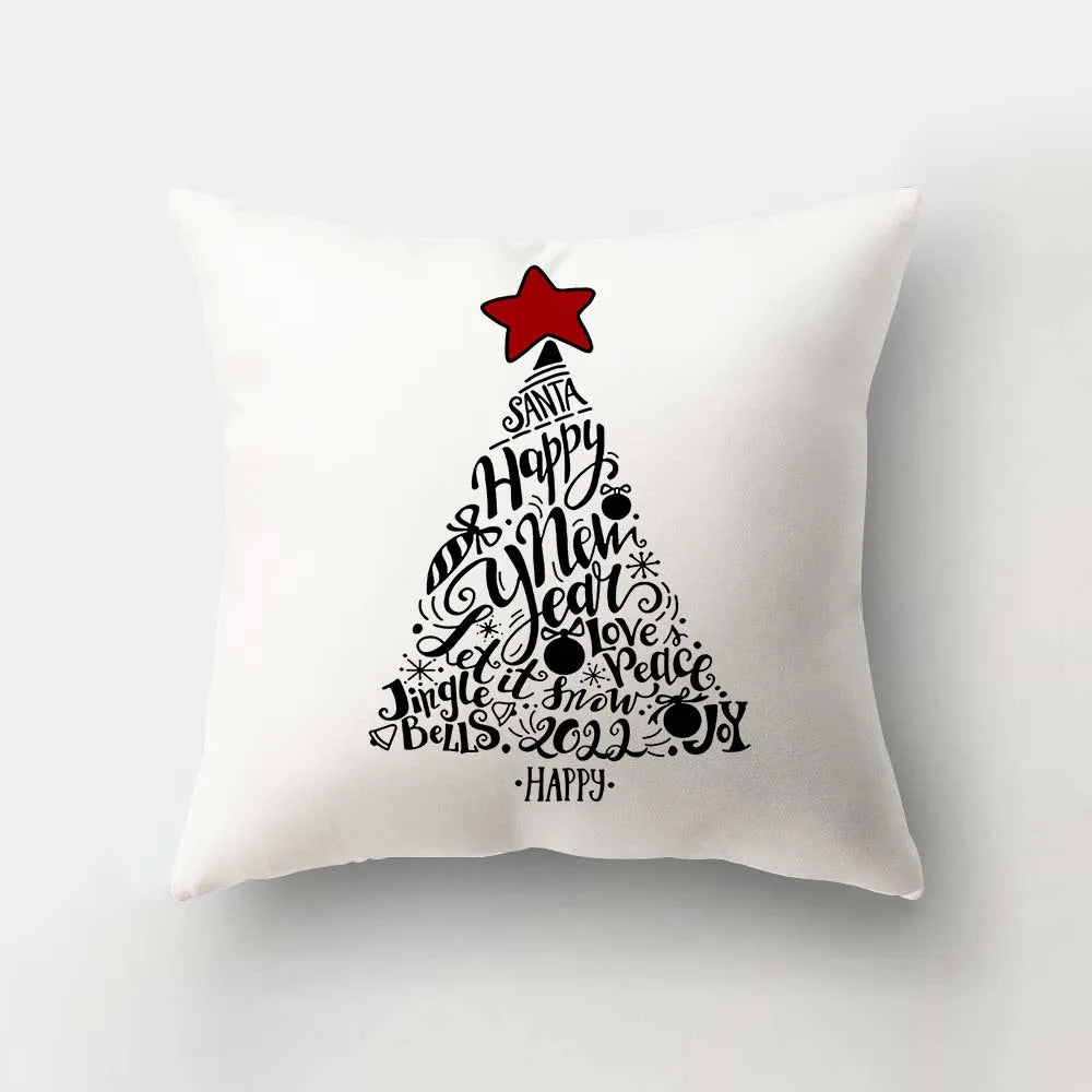 White pillow with a Christmas tree design made of festive words like "Santa," "Happy New Year," and "Joy" in black text, topped with a red star.