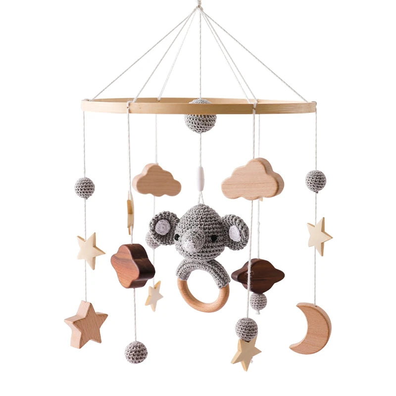 A wooden baby mobile featuring a crocheted elephant, stars, clouds, crescent moon, and textured balls hanging from strings, all suspended from a circular wooden frame.