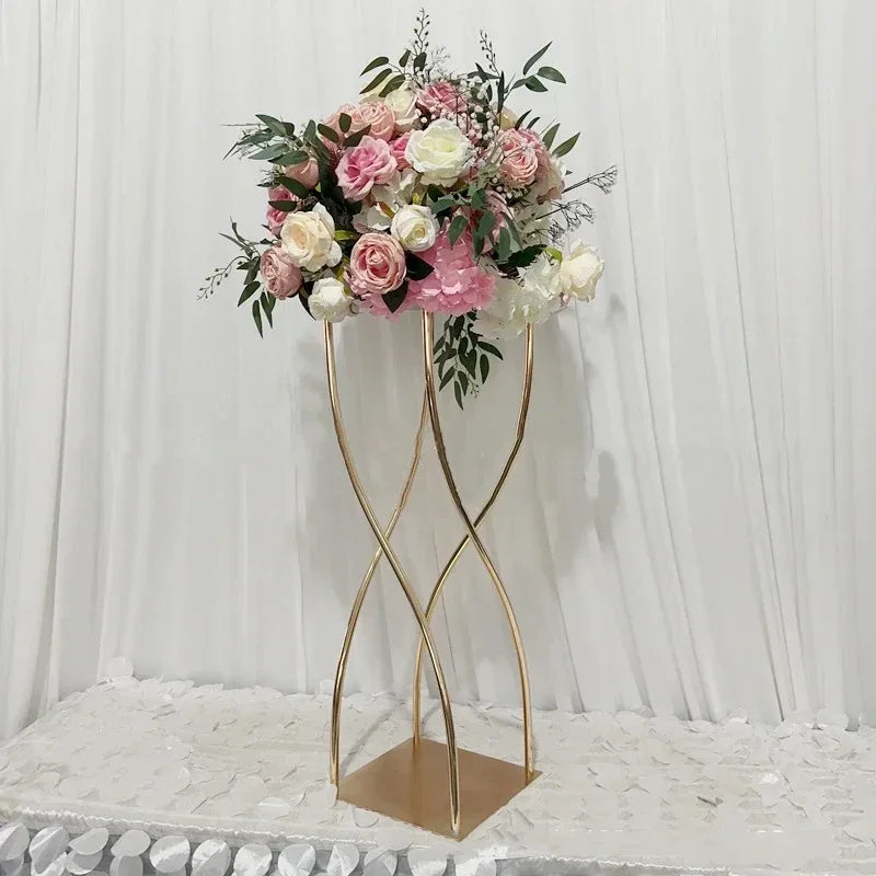 Elegant floral arrangement with pink and white roses on a gold twisted stand, set against a white draped background on a petal-covered table.