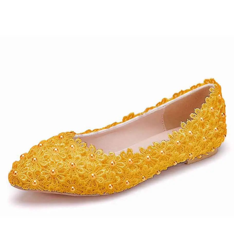 Yellow flat shoe adorned with intricate floral lace and small pearls, featuring a pointed toe. The shoe has a beige interior and a low heel, showcasing elegant detailing.