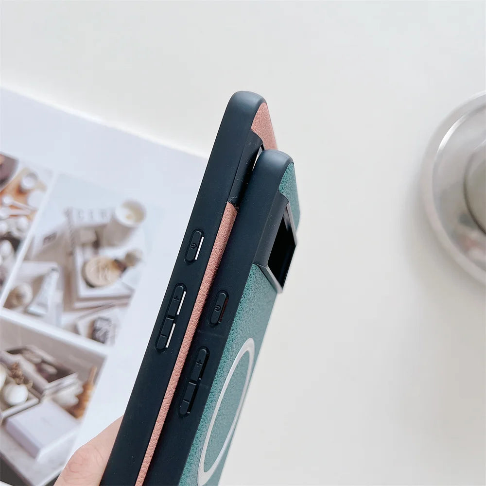 Two smartphones with protective cases, one green and one pink, are held close together. The cases feature side buttons and a circular design. Books and candles appear in the blurred background.