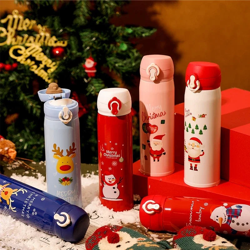 Festive thermos bottles with Christmas designs featuring reindeer, snowmen, and Santa Claus are arranged on a snowy table. A decorated Christmas tree is in the background.