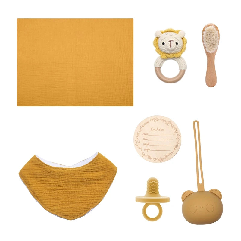 Yellow baby gift set includes a teether with lion face, soft brush, bib, silicone pacifier with bear case, muslin cloth, and wooden birth announcement disc.