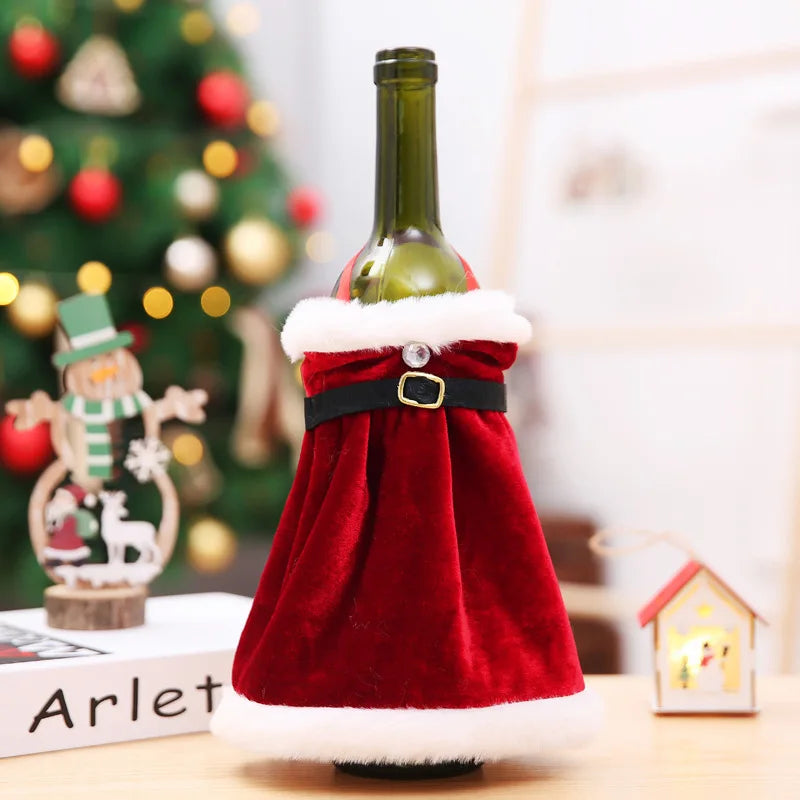 A wine bottle dressed in a red Santa coat with white fur trim and a black belt. It's set against a blurred background with holiday decorations, including a Christmas tree.