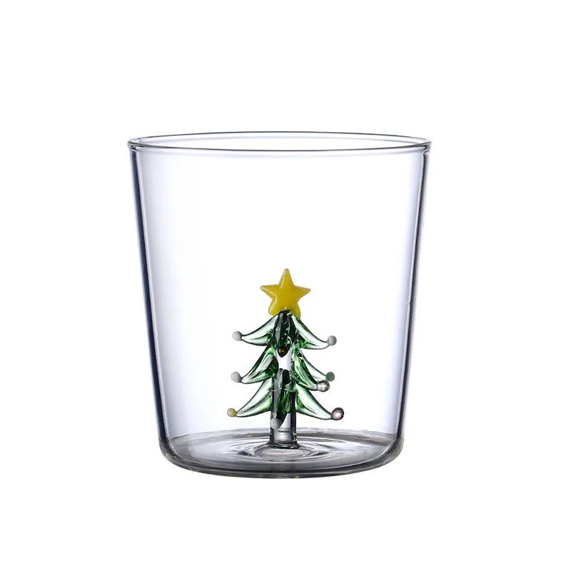 A clear glass with a small, decorative glass Christmas tree inside, topped with a yellow star, sits on a white background.