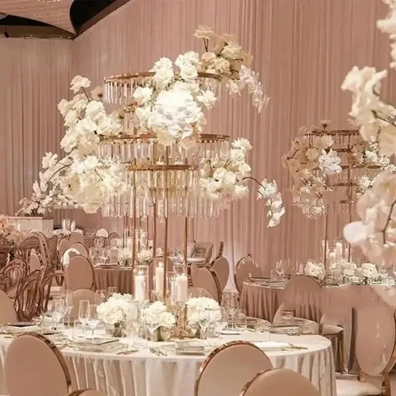 Elegant wedding reception with round tables elegantly set with white floral centerpieces and gold chairs, under soft pink lighting and tall crystal candle holders.