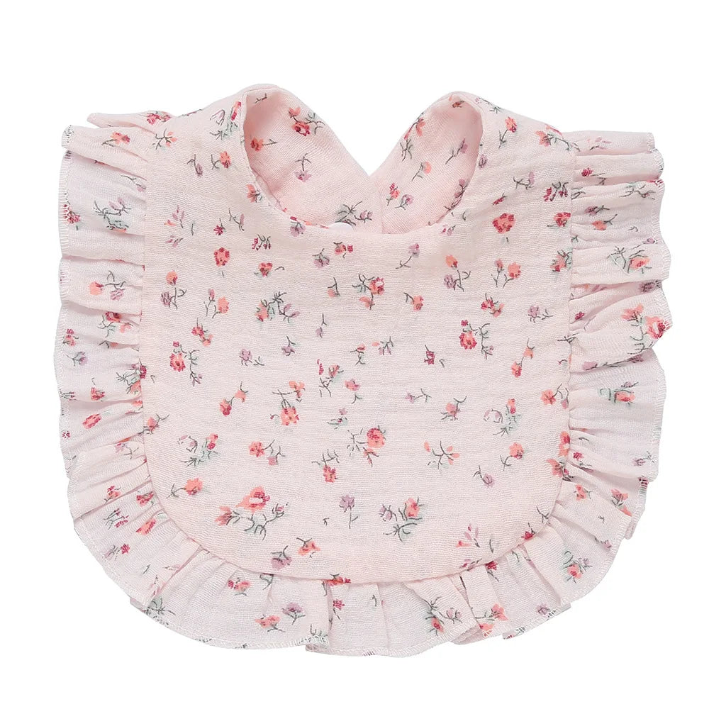 Pink floral baby bib with ruffled edges. The fabric features small, scattered flowers in various shades of pink and green, giving it a delicate and charming appearance.