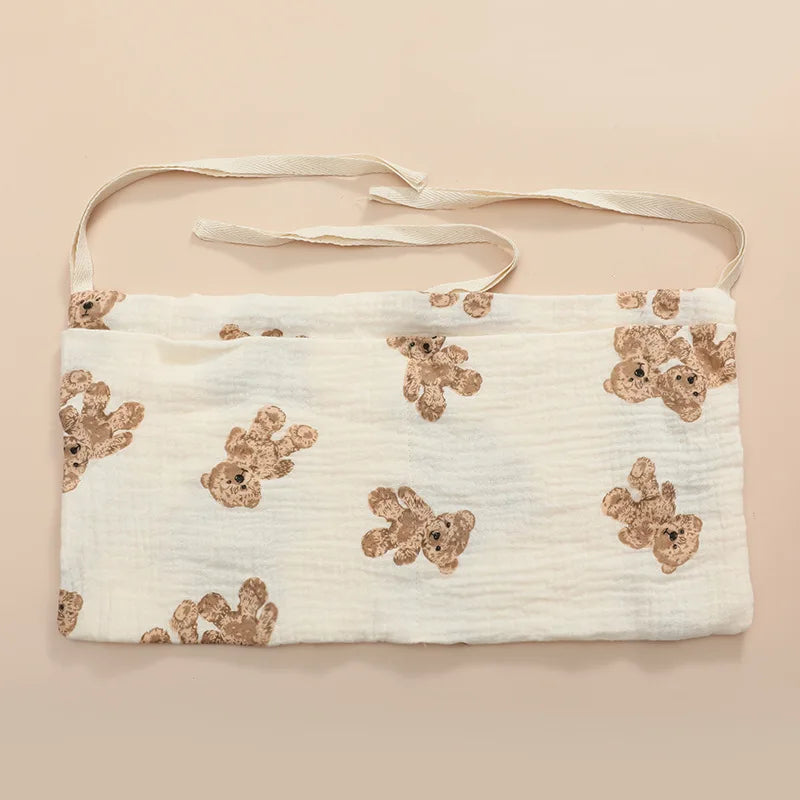 White fabric bib with brown teddy bear patterns and tie strings, displayed on a beige background.
